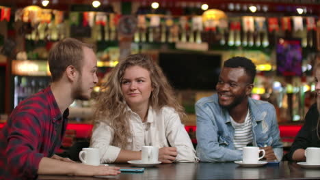 Student-meeting-in-a-restaurant-and-cafe.-A-man-in-a-shirt-tells-a-story-to-friends-two-girls-and-an-African-American-are-listening-and-laughing.-A-group-of-friends-spend-time-together